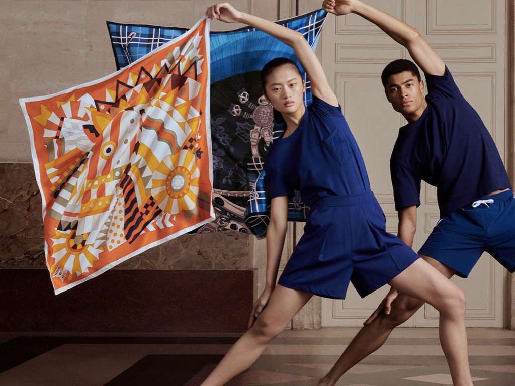 Imagem da campanha de lenços da Hermés. Dois modelos seguram dois lenços estampados da marca.