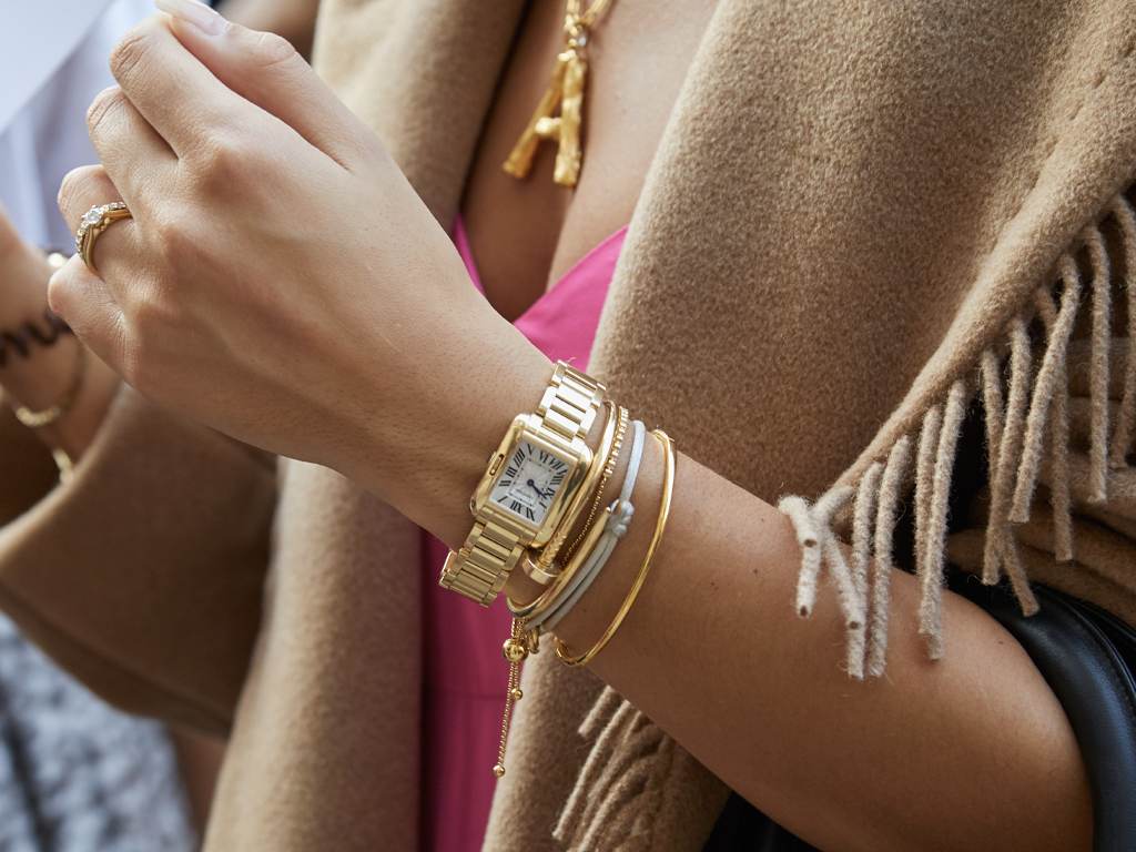 Imagem com modelo usando muitas jóias douradas e prateadas combinadas com relógio de luxo.