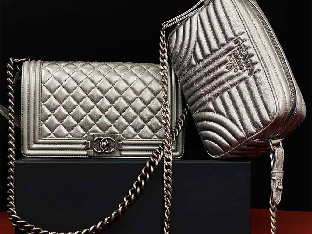 Imagem com duas bolsas prateadas,sendo uma da marca Chanel e a outra da Prada.