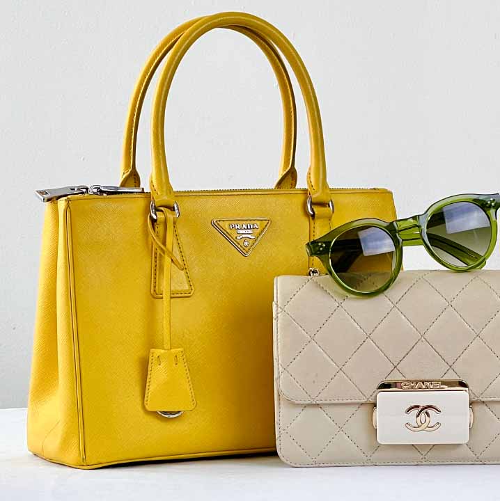 Foto de uma bolsa Chanel ao lado de uma bolsa amarela Prada e um óculos de sol.