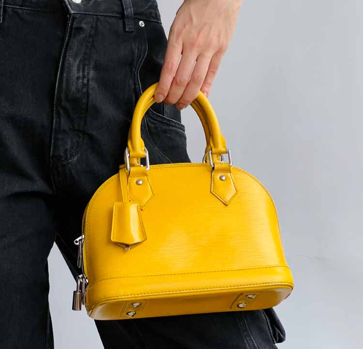 Foto de uma mulher segurando uma das tote bags mais famosas da Louis Vuitton: a bolsa de mão Alma.