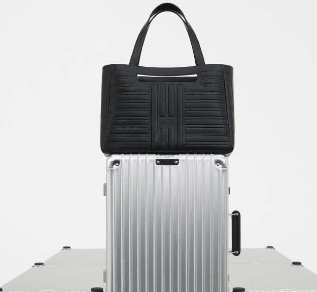 Foto de bolsa de couro da Rimowa em cima de uma mala de alumínio da marca alemã.