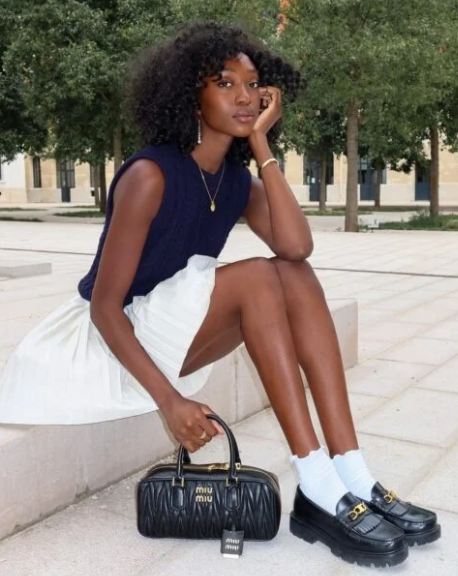 Foto de uma mulher usando mocassim tratorado com saia curta e meias brancas.