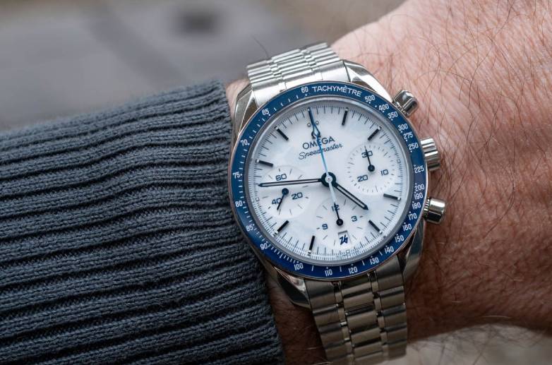 Omega Speedmaster 38mm Milano Cortina 2026 com luneta em cerâmica azul e mostrador branco texturizado.