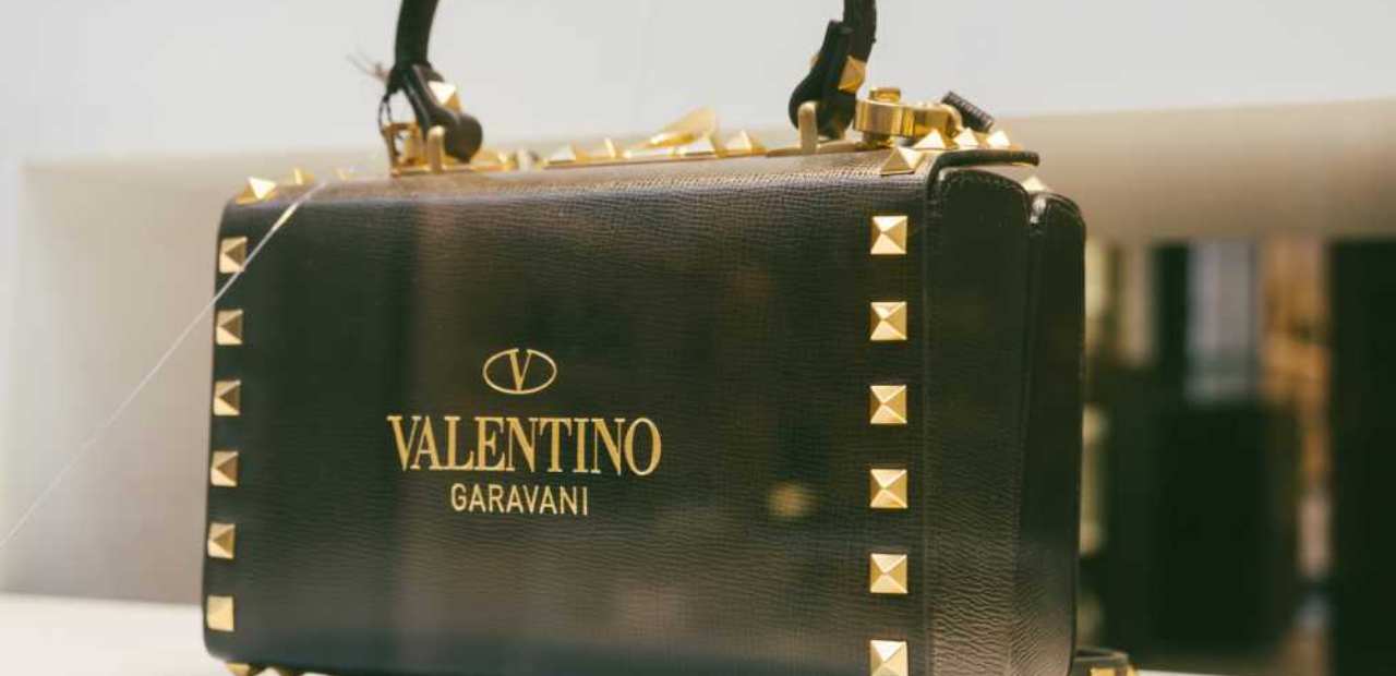 Valentino é a maison; Valentino Garavani é a linha de acessórios. Entenda a diferença, o que mudou em 2026 com Alessandro Michele e onde comprar original no Brasil.